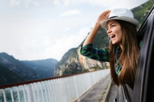 Woman in car on road trip waving out the window and smiling