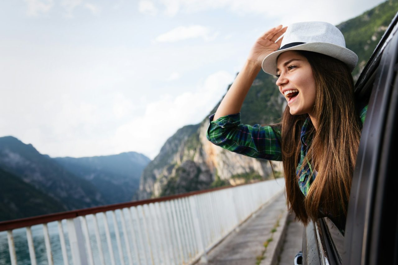 Woman in car on road trip waving out the window and smiling